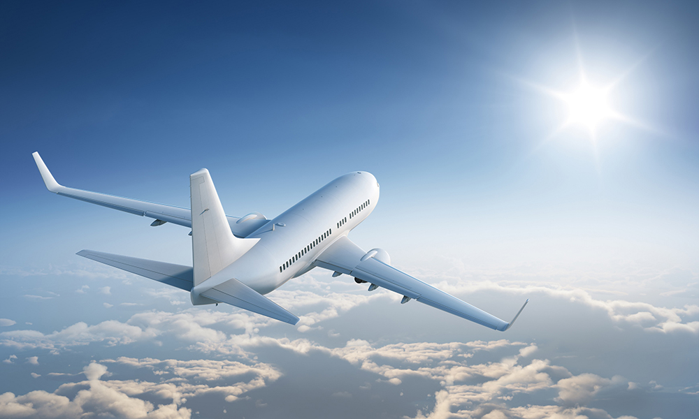 Airplaine flies above the calm cloudscape towards the sun.